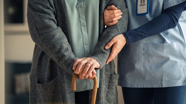 Finding the perfect home for aging parents in Columbus. Image of an elderly person with a cane and a worker healping to steady their arm.